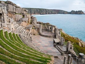 Ein Steine Amphitheater mit terrassenförmigen Sitzreihen und einer Bühne, das auf eine Küstenlandschaft blickt.