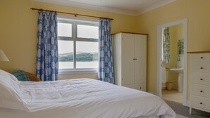 Un dormitorio con cama, armario, ventana con cortinas y baño visible a través de una puerta abierta.