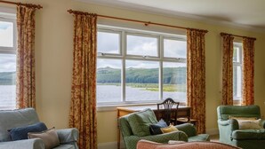 Una habitación con vistas a un lago, una mesa de madera y dos sillones verdes.