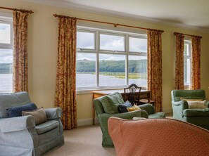Ein Zimmer mit Seeblick, einem Holztisch und zwei grünen Sesseln.