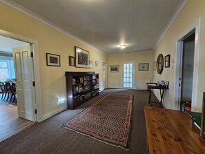 Ein geräumiges Wohnzimmer mit großem Teppich, einer Bücherwand und einem Essbereich, der durch eine offene Tür sichtbar ist.