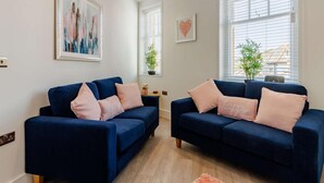 Ein modernes Wohnzimmer mit zwei dunkelblauen Sofas, einem pinkfarbenen Teppich und Kunstwerken an den Wänden.