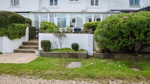Ein zweistöckiges Haus mit Wintergarten, einem Vorgarten mit Hecken und einem Schotterweg.