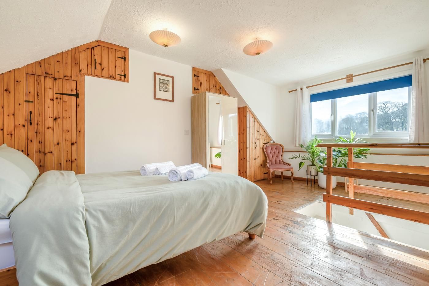 A bedroom with a bed, towels, a chair, a window, and a staircase.