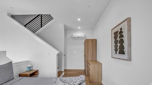 A bedroom with a bed, a nightstand, a wooden wardrobe, a staircase, and an air conditioning unit. - Rino Private Rooftop  - Art District Location. Walk To Everything! (Denver)
