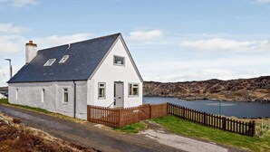 A white house with a dark roof, a wooden fence, and a body of water in the background. - 4 Bed in Scourie (oc-ca399) (Scourie More)