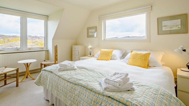 A bedroom with a bed, two bedside tables, a chair, a window with a view, and a ceiling light. - 4 Bed in Scourie (oc-ca399) (Scourie More)
