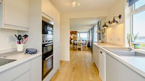 A modern kitchen with white cabinets, a built-in oven, and a dining area with a view. - 4 Bed in Scourie (oc-ca399) (Scourie More)