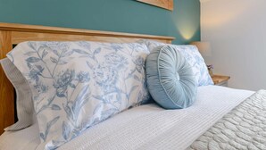 A bed with floral bedding, a wooden headboard, and a nightstand with a lamp. - 2 Bed in York (oc-81052) (Helmsley)