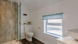 Ein Badezimmer mit Duschkabine aus Glas, Toilette, Fenster mit gemustertem Vorhang und weißem Waschbecken.