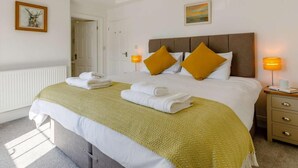 Ein Hotelzimmer mit einem Bett, zwei Nachttischlampen, einem Nachttisch, einem gerahmten Bild an der Wand und einer Tür zu einem anderen Raum.