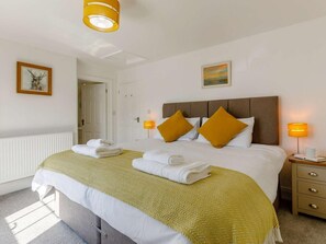 Ein Hotelzimmer mit einem Bett, zwei Nachttischlampen, einem Nachttisch, einem gerahmten Bild an der Wand und einer Tür zu einem anderen Raum.