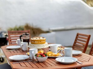 A wooden dining table set with plates, cutlery, a bowl of fruit, and a cake. - 3 Bed in Bideford (oc-65162) (Instow)