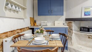 A compact kitchen with blue cabinets, a white countertop, and a dining table set for four. - 2 Bed in Brixham (oc-bx087) (Brixham)