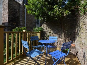 Ein Steinhaus mit einer Holzdielen-Terrasse, blauen Stühlen und einem kleinen, runden Tisch.