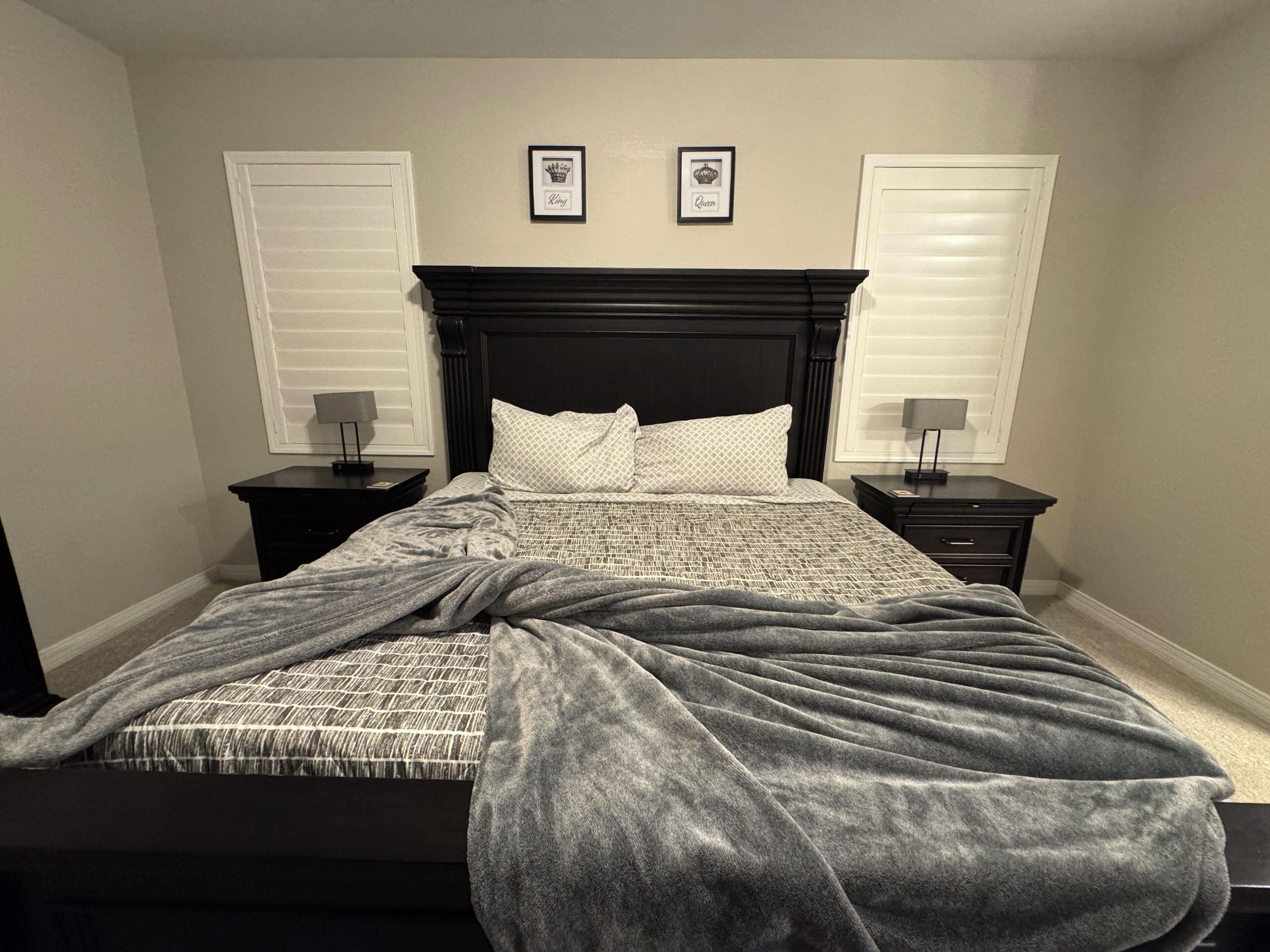 Une chambre à coucher comprenant un lit, deux tables de chevet, une tête de lit et deux tableaux encadrés accrochés au mur.
