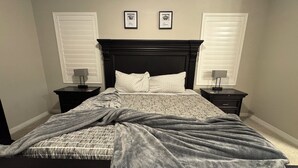 Une chambre à coucher comprenant un lit, deux tables de chevet, une tête de lit et deux tableaux encadrés accrochés au mur.