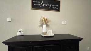 Une commode noire avec des tiroirs, un panneau encadré placé au-dessus, un vase contenant des plumes d’herbe des pampas et un petit panneau blanc posé sur la commode.