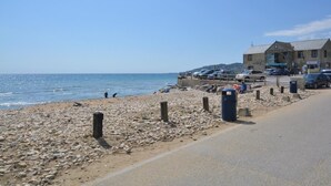 Une route côtière bordée d’une plage de galets, un bâtiment avec une enseigne et des voitures garées.