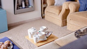 Ett mysigt vardagsrum med en beige soffa, ett soffbord med vita koppar och en tekanna, och en inramad tavla på väggen.