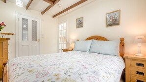 Une chambre à coucher avec une couvre-lit à motifs floraux, une tête de lit en bois, des tables de chevet avec des lampes, une armoire et deux tableaux à motifs floraux encadrés accrochés au mur.