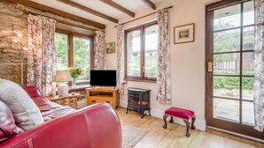 Un salon chaleureux avec un canapé en cuir rouge, un téléviseur, une table en bois et un mur en pierre.