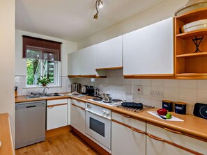 A compact kitchen with white cabinets, a built-in oven, a dishwasher, and a window with a view of greenery. - 1 Bed in Ambleside (oc-94656) (Grasmere)