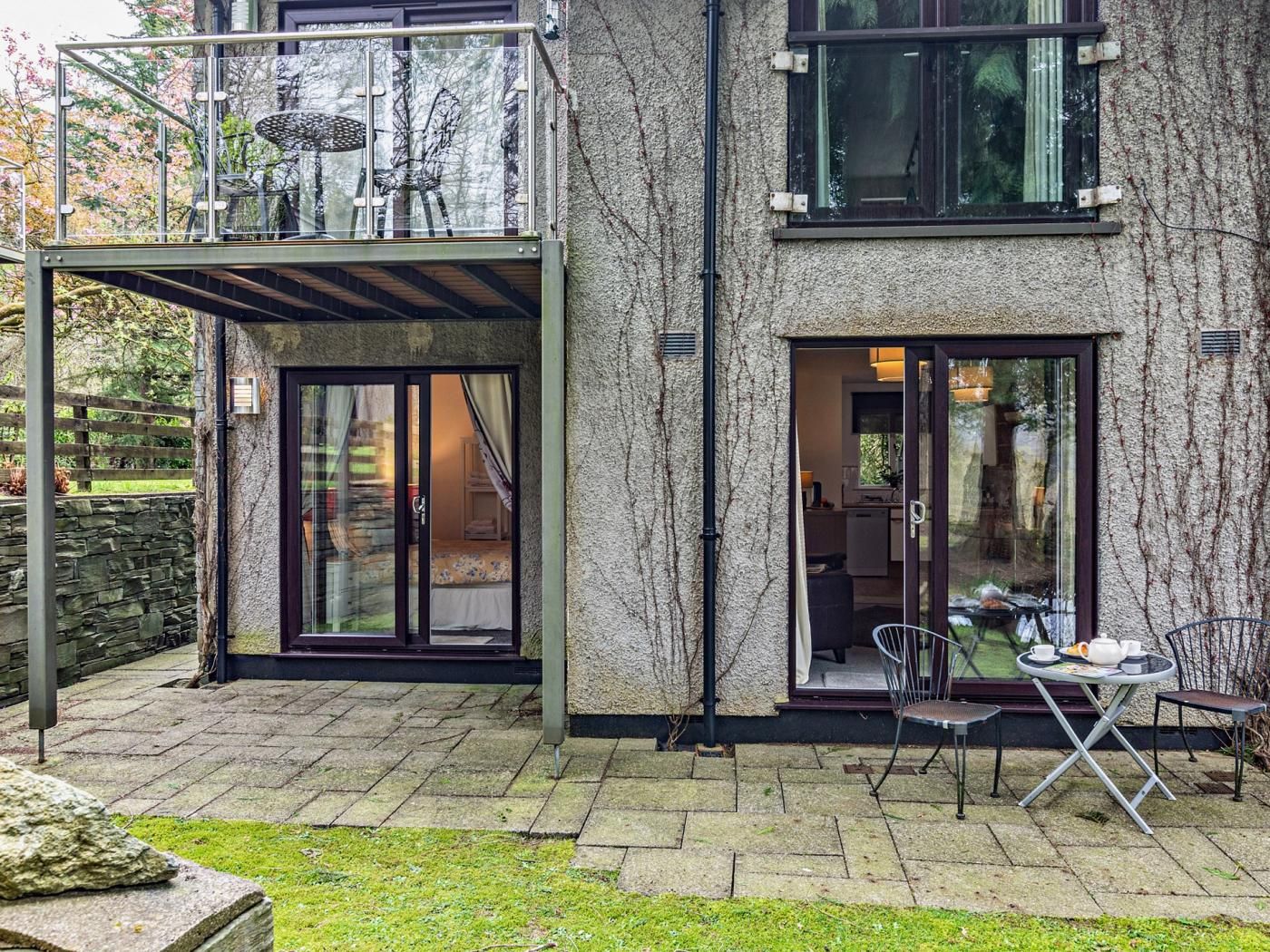 Et moderne hus med en glasbalkon, en terrasse med bord og stole, samt en stenvæg.
