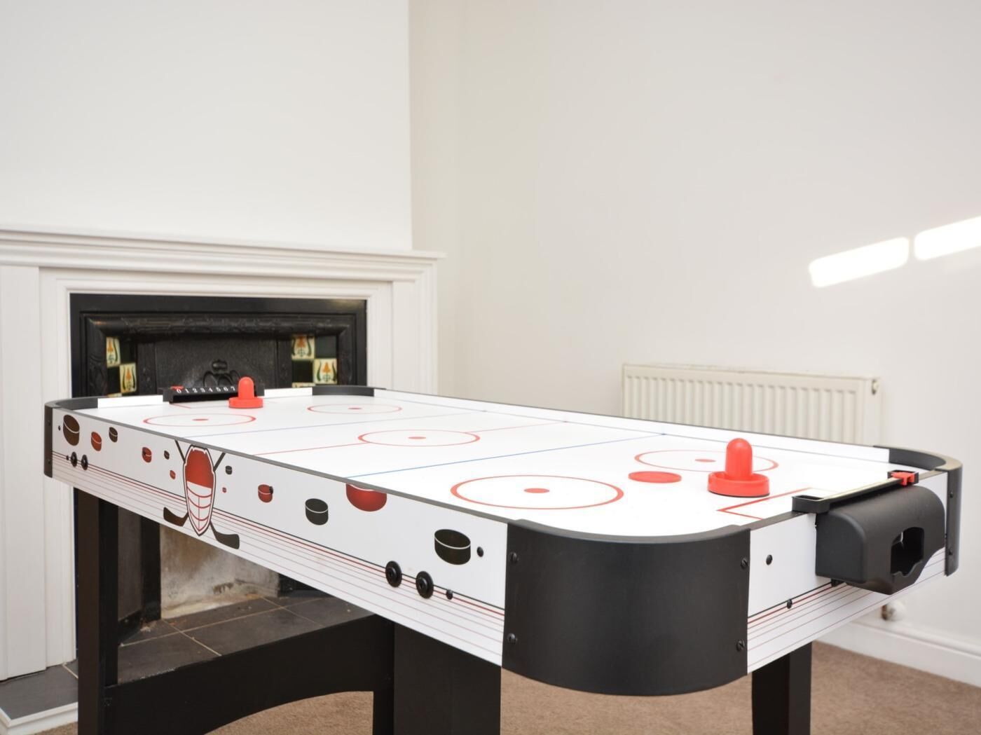 Une table de baby-foot dans une pièce avec une cheminée, un radiateur et un sol carrelé.