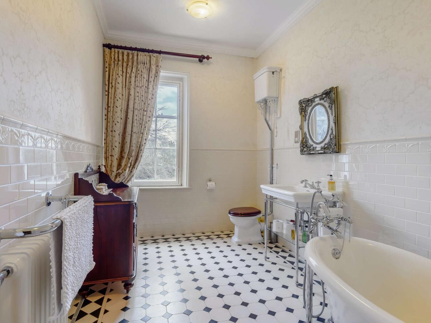 Een badkamer met een bad, toilet en raam met gordijnen.