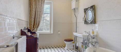 Een badkamer met een bad, toilet en raam met gordijnen.