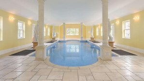 Ein großes, überdachtes Schwimmbecken mit klassischen Säulen, gelben Wänden und einem gefliesten Boden.