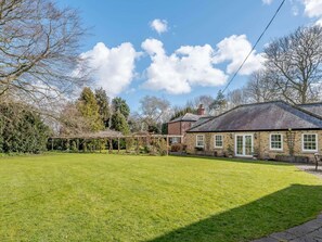 Une maison avec une pelouse bien entretenue, une façade en briques et un jardin agrémenté d’une pergola.