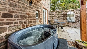 Un bâtiment en pierre doté d’un jacuzzi, d’un espace salon extérieur et d’une pergola en bois.