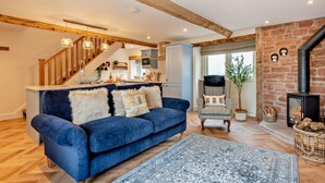 Un salon chaleureux avec un canapé bleu, un tapis à motifs, un escalier en bois, un coin cuisine et une cheminée.