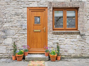 Una porta de fusta amb un petit finestret a la part superior, emmarcada per plantes en testos.