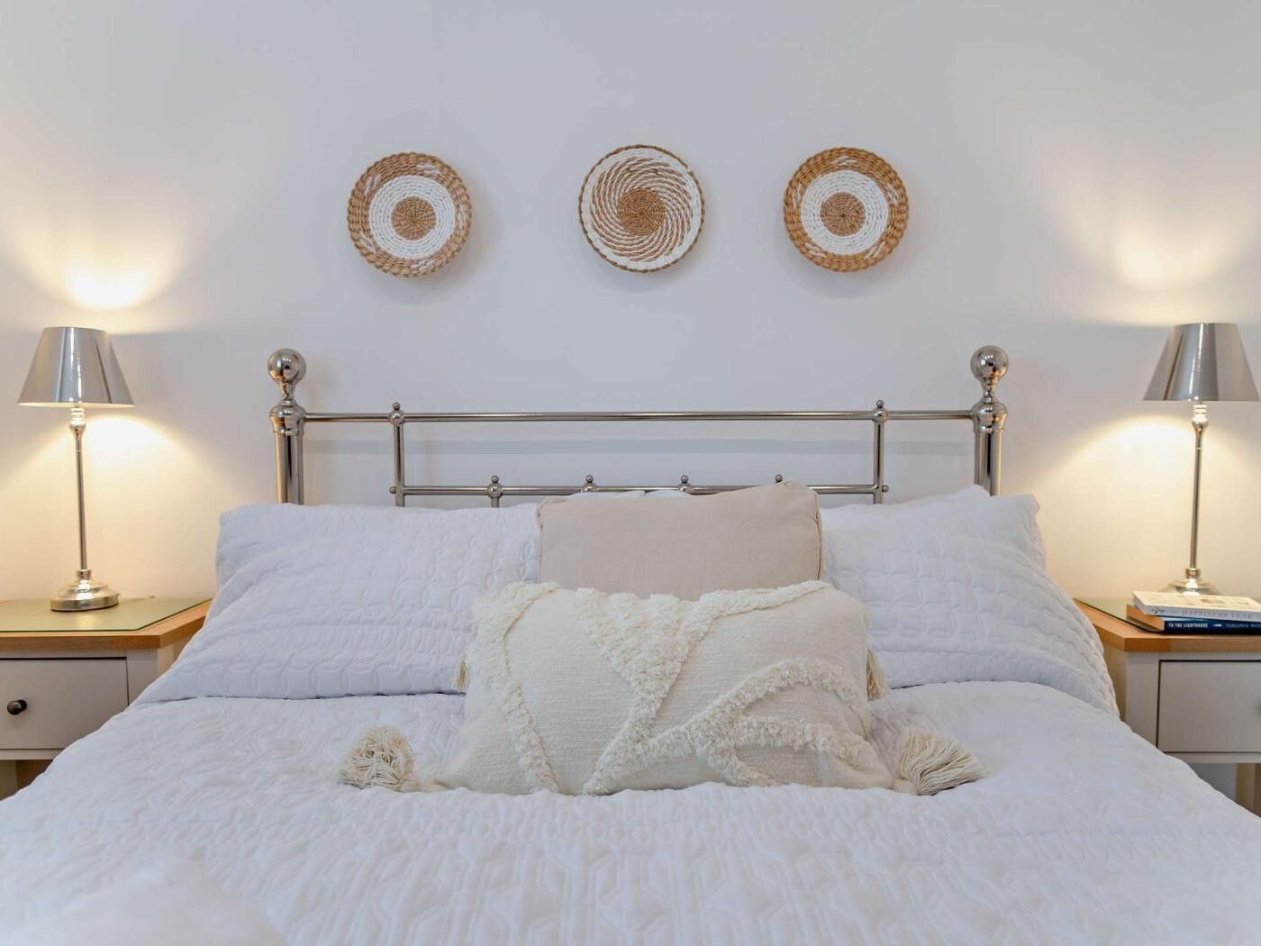 A bed with a metal frame, white bedding, and three woven wall decorations.