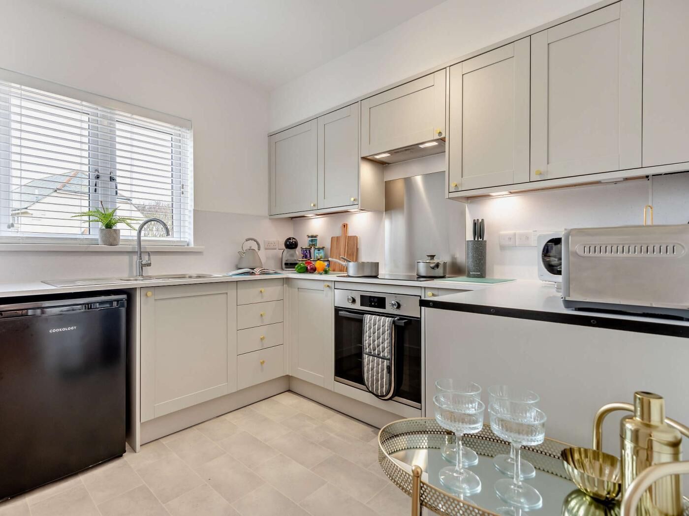 A modern kitchen with a dishwasher, oven, and a window with blinds.