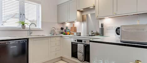 A modern kitchen with a dishwasher, oven, and a window with blinds.