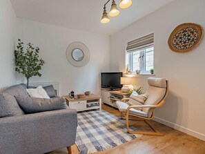 En stue med sofa, stol, fjernsyn, sofabord, en plante og et vindue med persienner.