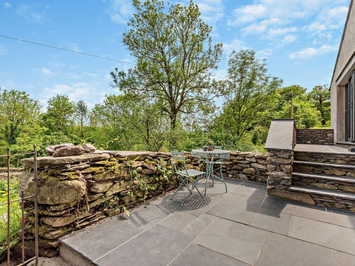 Une terrasse avec des murs en pierre, une table en métal et une chaise.