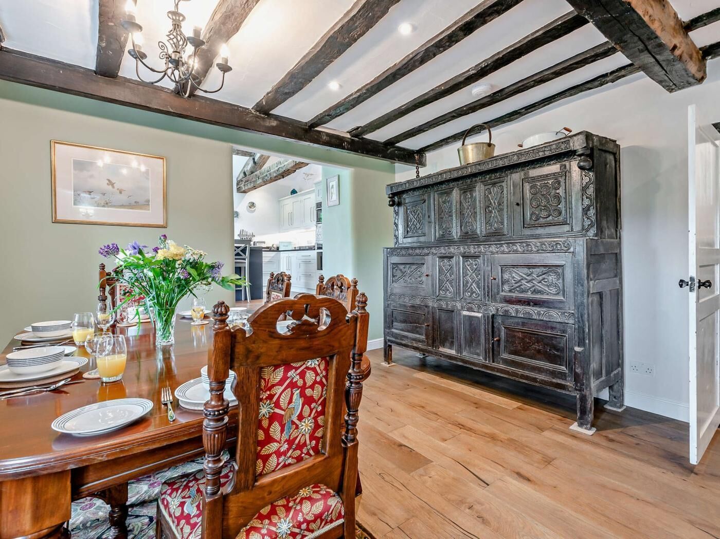 Un coin repas avec une table en bois dressée pour quatre personnes, un vase rempli de fleurs et une cheminée rustique.