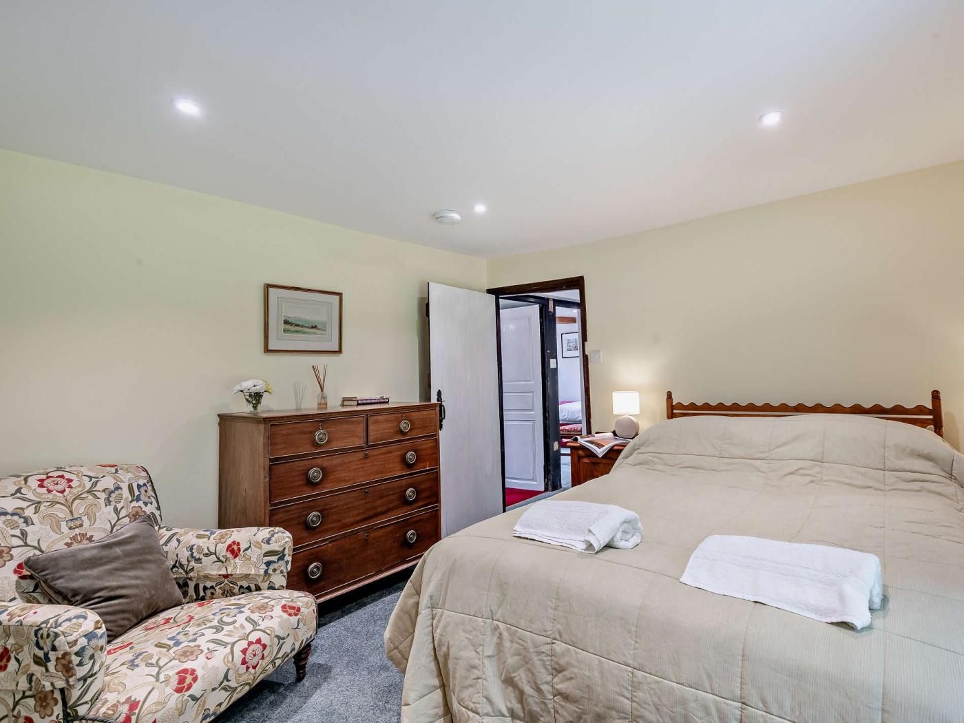 Quarto com cama, cômoda, cadeira e porta que dá para outro espaço.