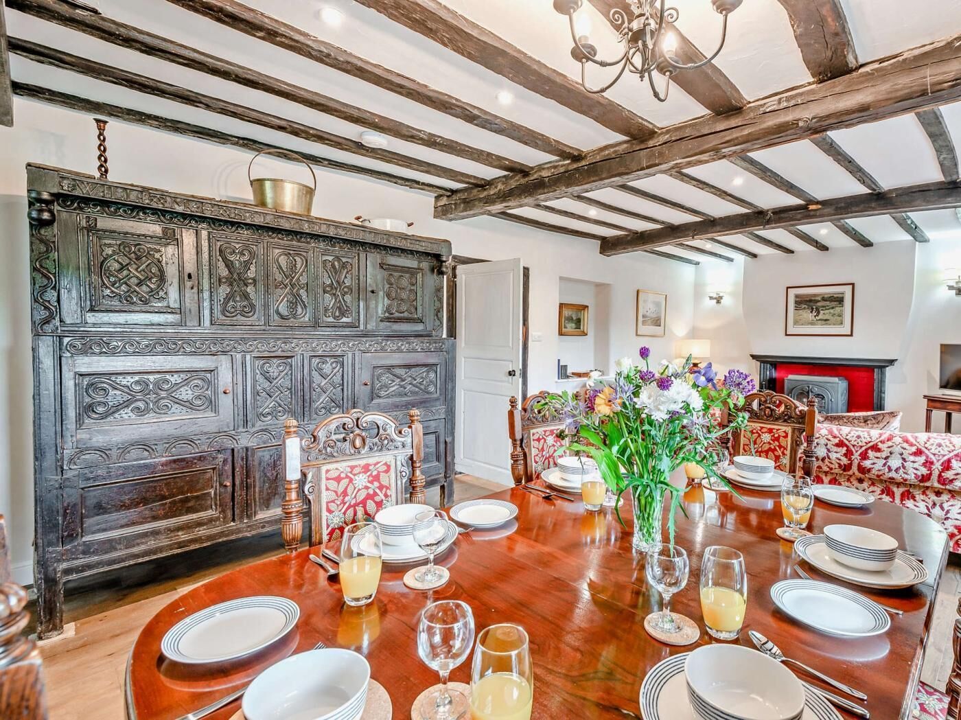 Comedor con mesa de madera dispuesta para seis comensales, una puerta grande y ornamentada, y una chimenea al fondo.