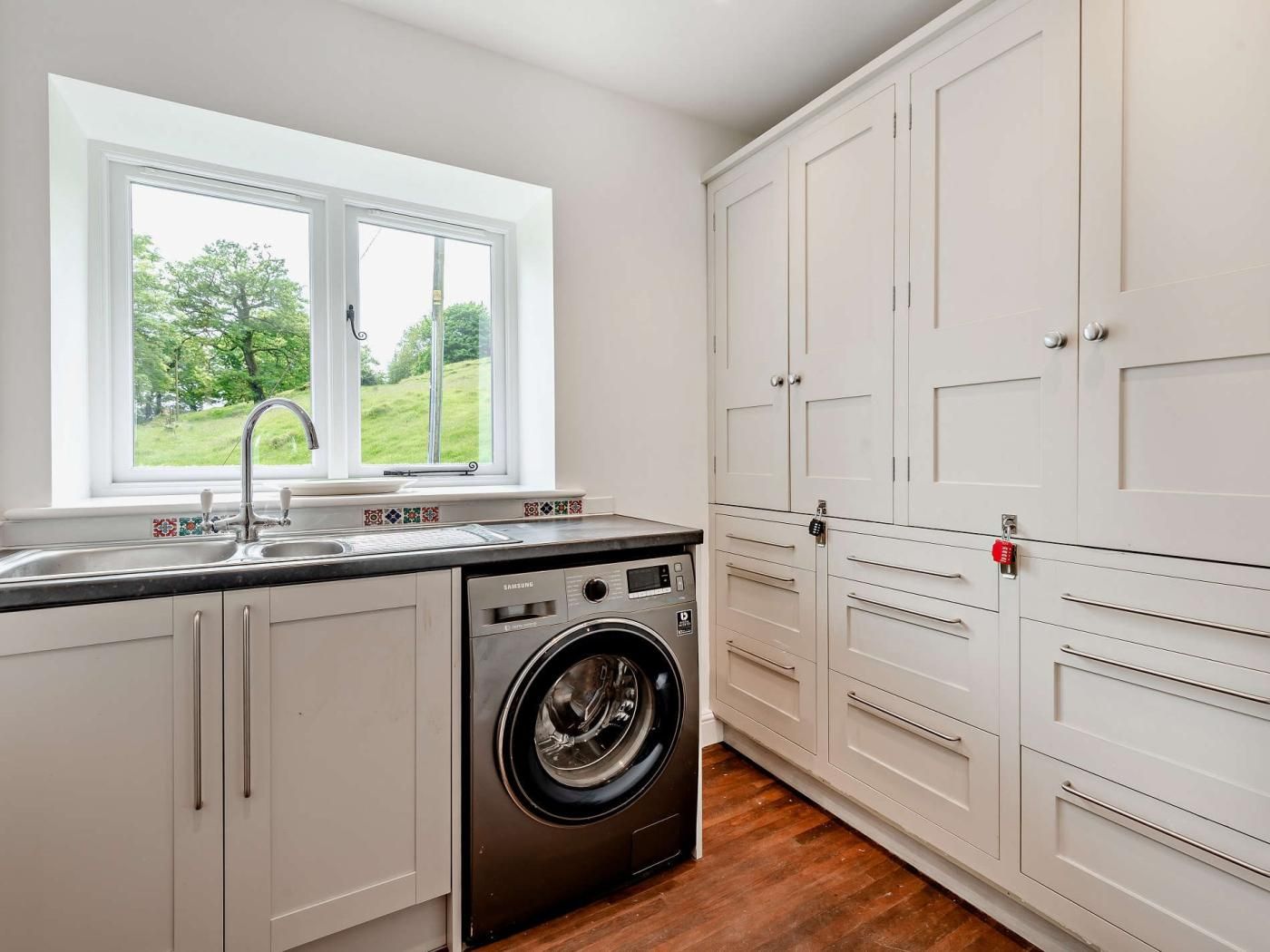 A kitchen with a built-in washing machine, a window with a view of greenery, and white cabinetry.