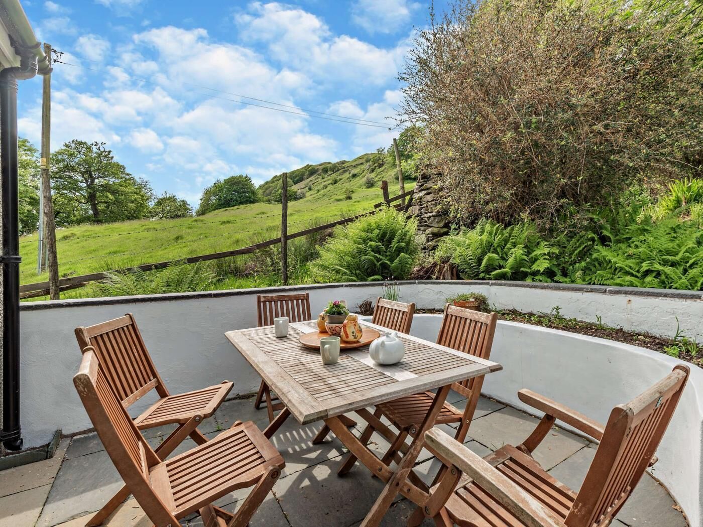 Une terrasse avec une table et des chaises, une vue sur un paysage verdoyant et un mur en pierre.