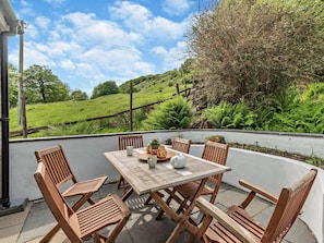 Eine Terrasse mit Tisch und Stühlen, Blick auf eine grüne Landschaft und eine Steinmauer.