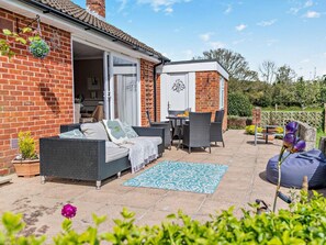 A patio with wicker furniture, a blue patterned rug, and a brick house with a white door. - 3 Bed in Christchurch (oc-94605) (Bransgore)