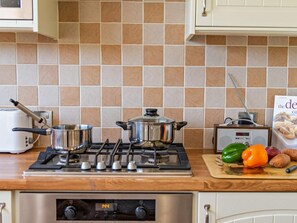 A kitchen with a stove, pots, a toaster, and a cutting board with vegetables. - 3 Bed in Christchurch (oc-94605) (Bransgore)