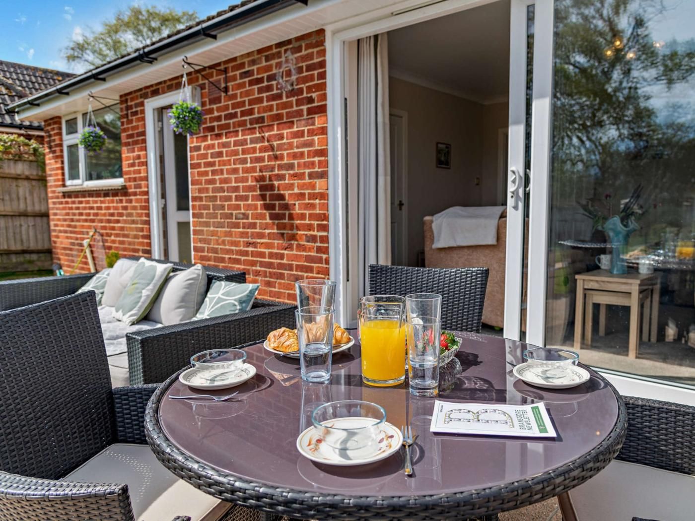 Une terrasse avec une table ronde, des chaises en osier et une table avec un plateau en verre.